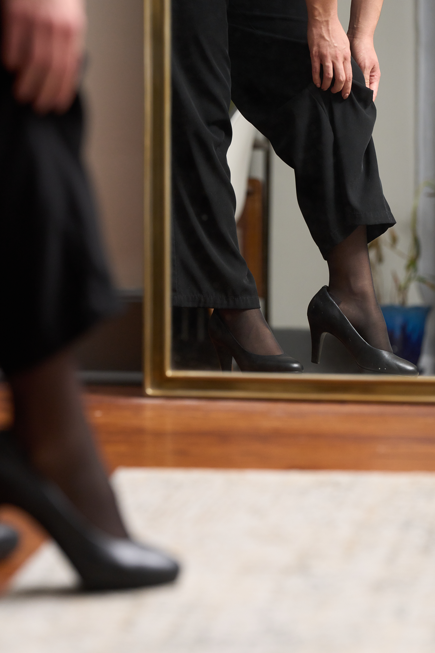 Person wearing black high heels and pants standing in front of a mirror.